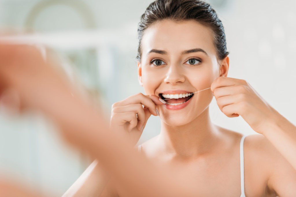mujer utilizando hilo dental manteniendo su higiene