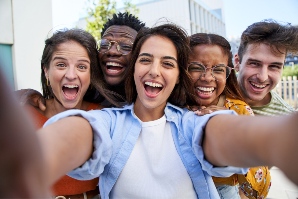 Un grupo diverso de jóvenes adultos sonríe y ríe en una foto grupal al aire libre.