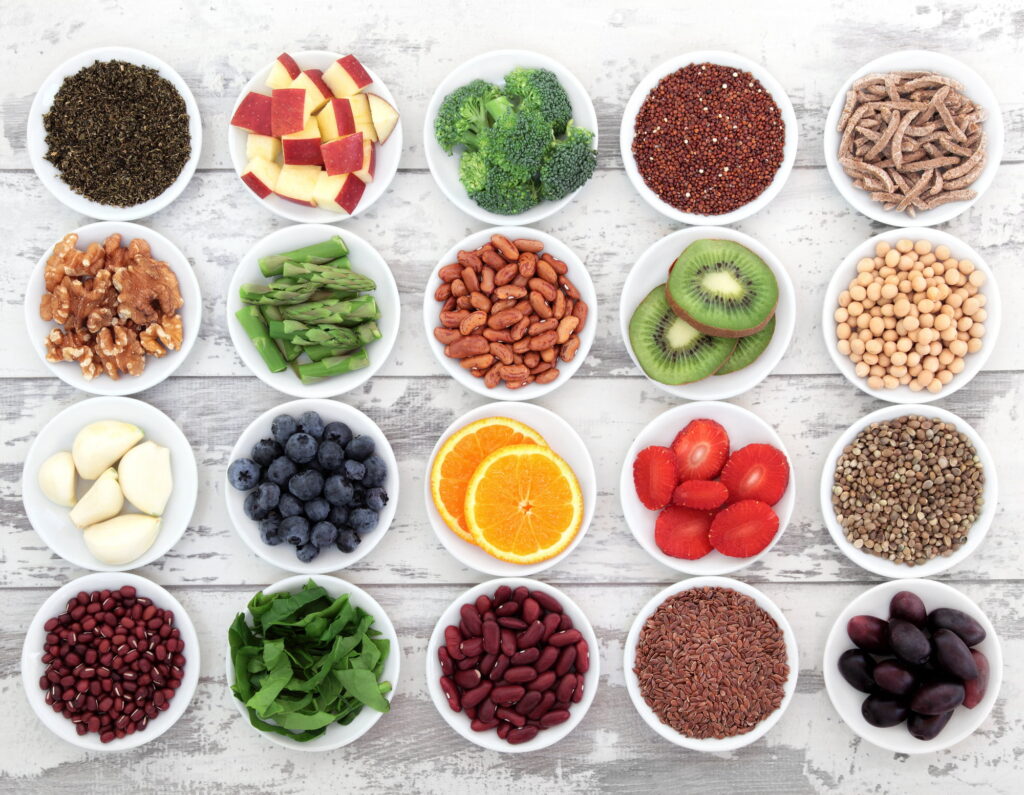 Variedad de alimentos saludables —frutos secos, legumbres, frutas, verduras y semillas— servidos en pequeños tazones.